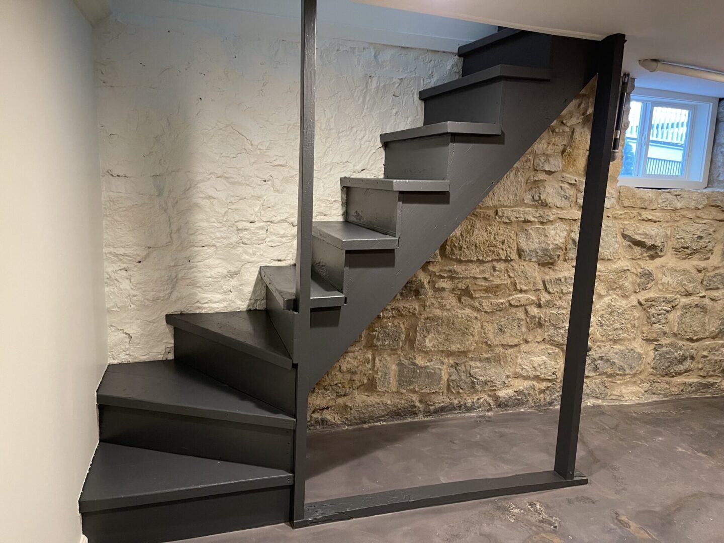 A black staircase in a room with a stone wall.