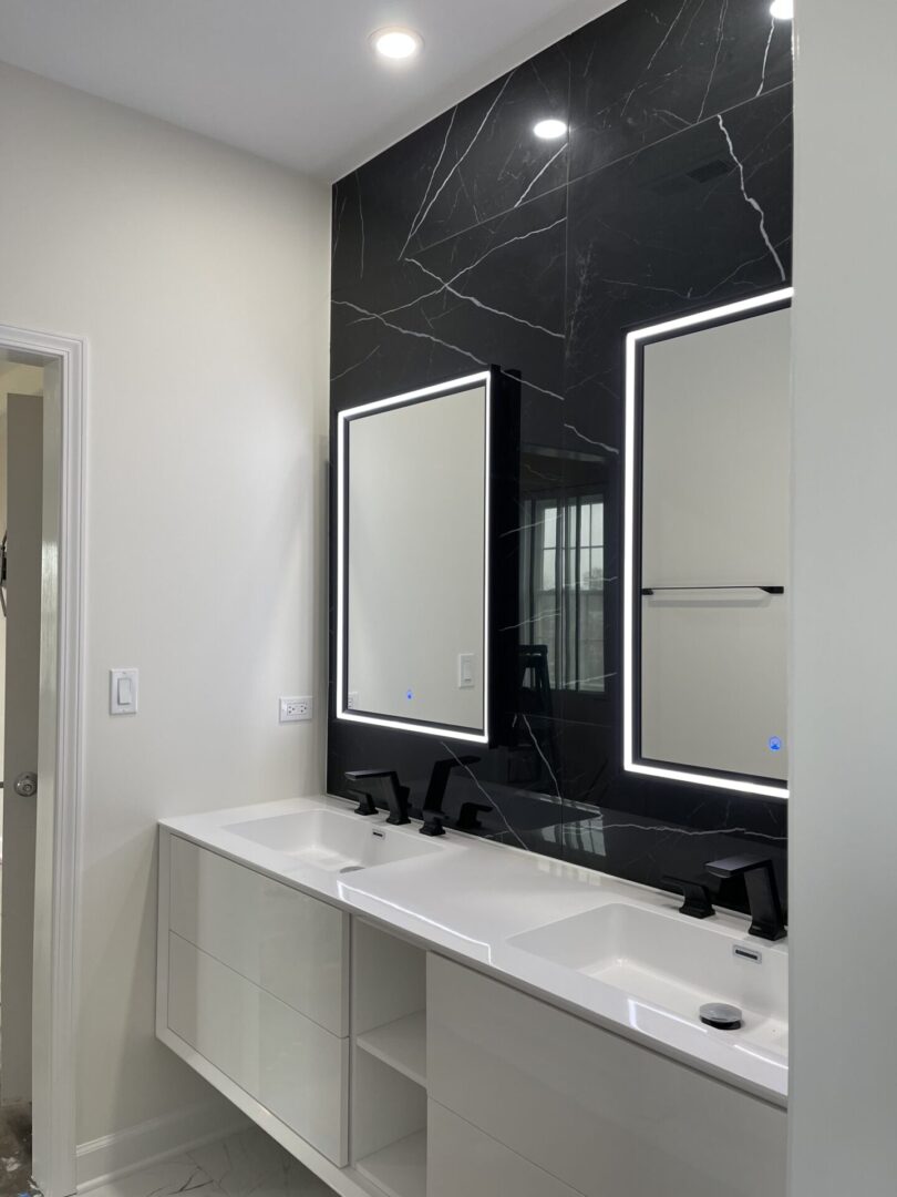 A modern bathroom with black marble counter tops and mirrors.