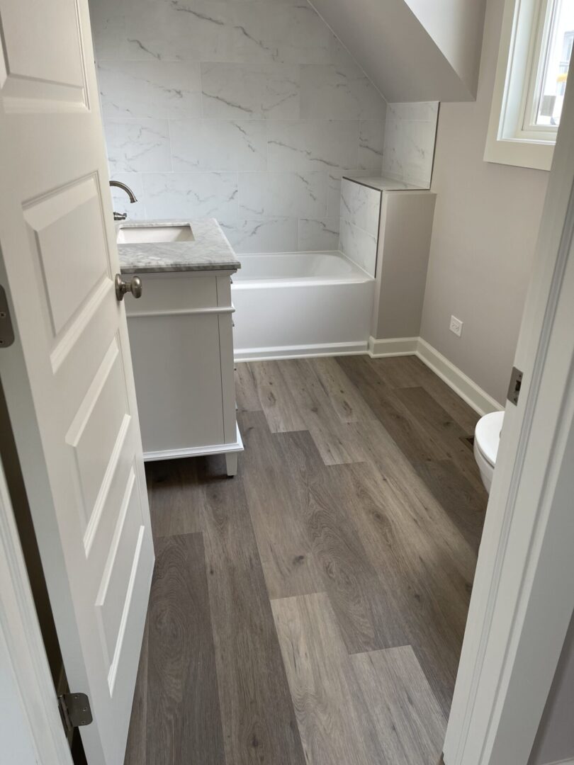 A bathroom with wood floors and a white tub.