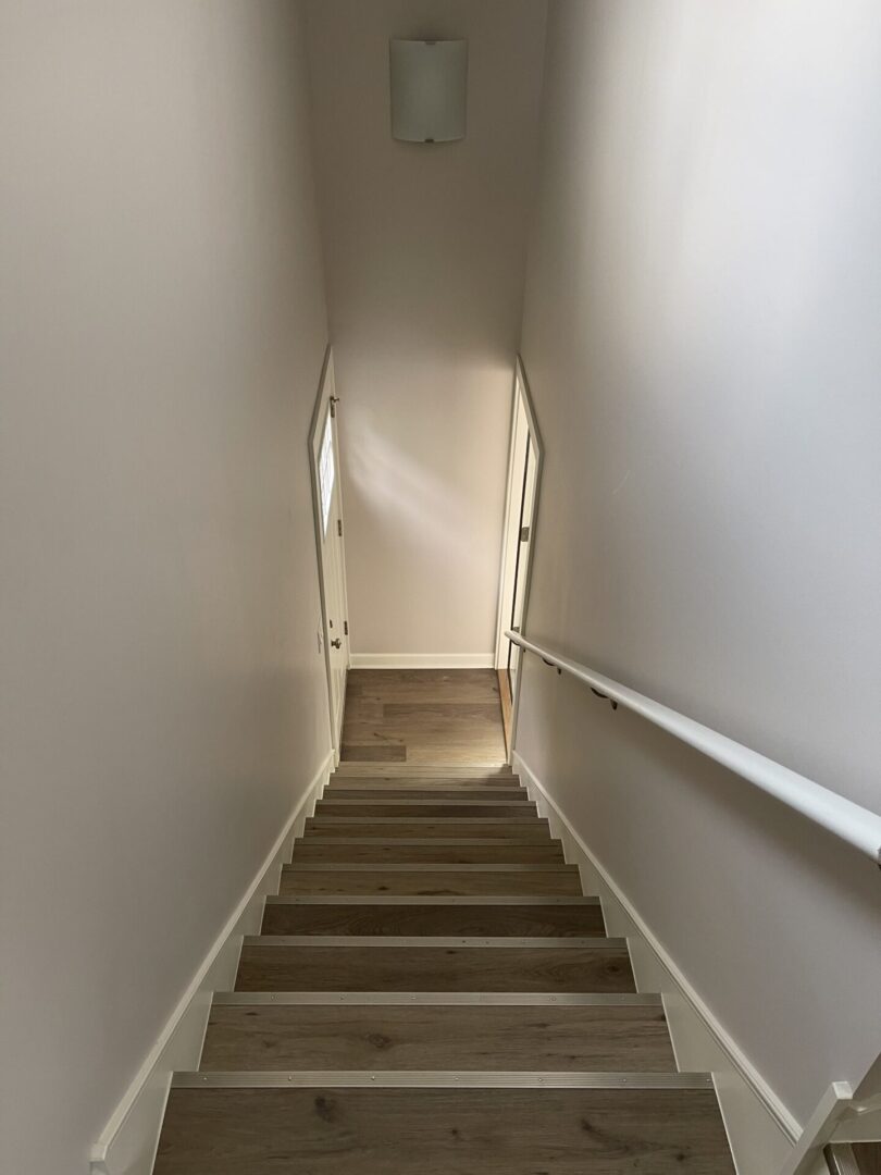 A stairway leading to a room with white walls and wood floors.