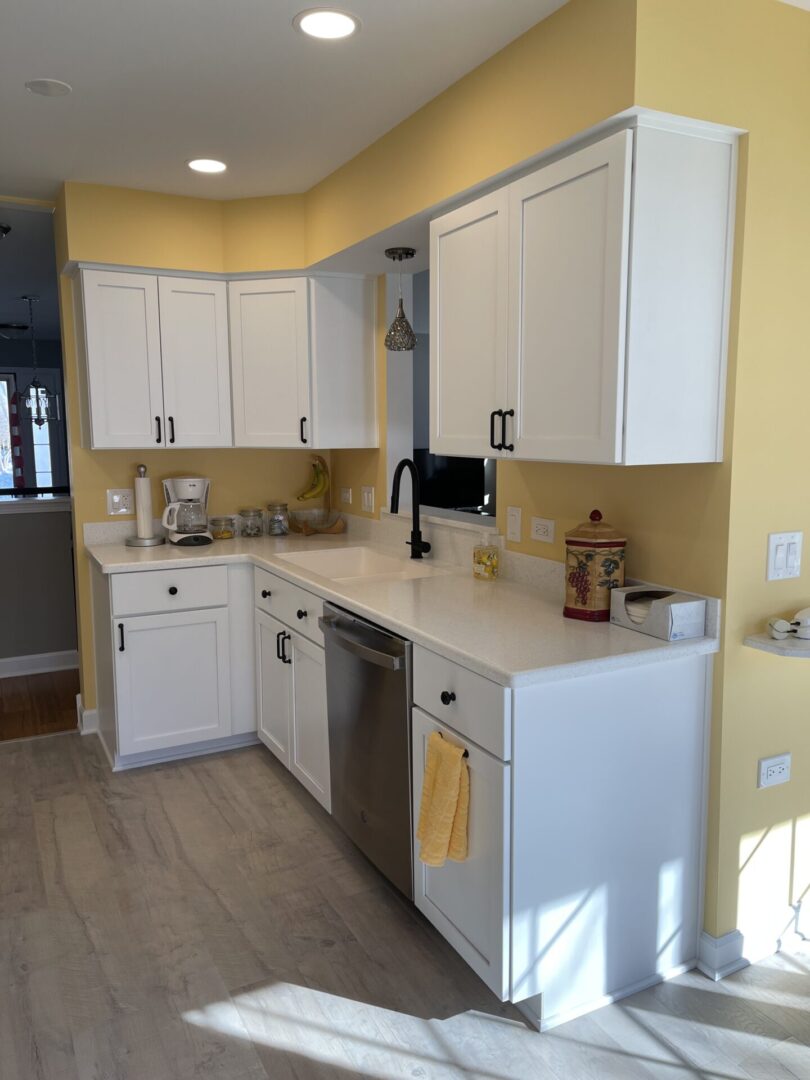 A kitchen with white cabinets and yellow walls.