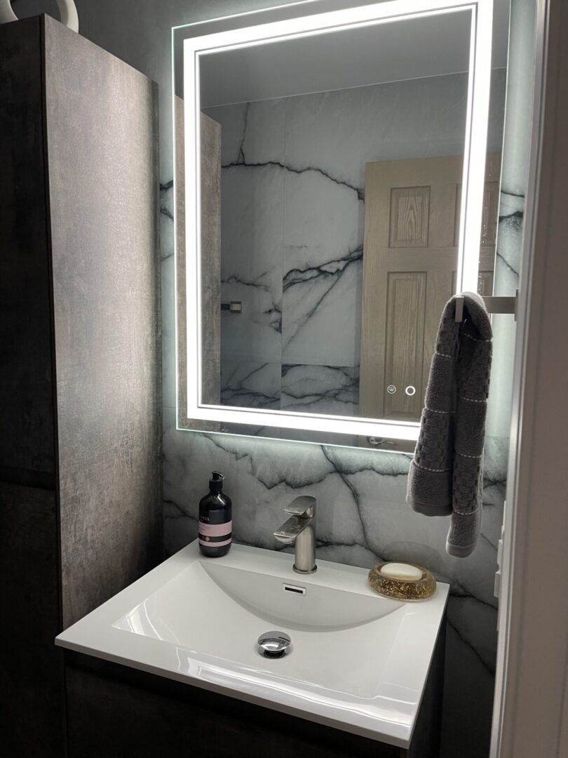 A bathroom with a marble vanity and lighted mirror.