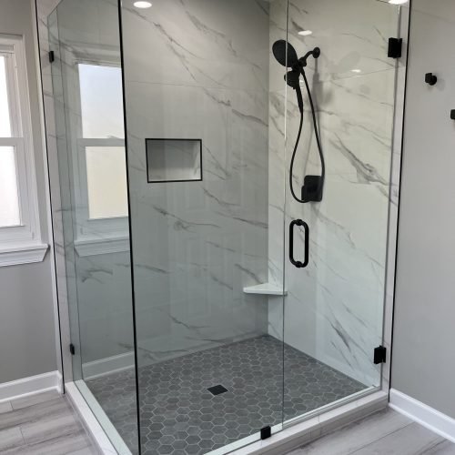 Walk-in glass shower enclosure with transparent panels, small tile walls and floor, and modern fixtures